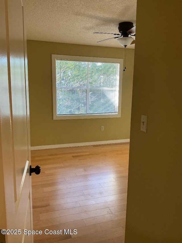 empty room with ceiling fan, a textured ceiling, a healthy amount of sunlight, and light wood-type flooring