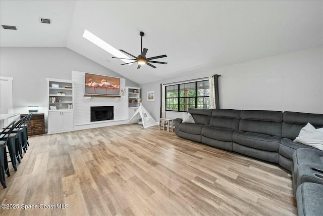 living room featuring a large fireplace, vaulted ceiling with skylight, ceiling fan, and light hardwood / wood-style flooring