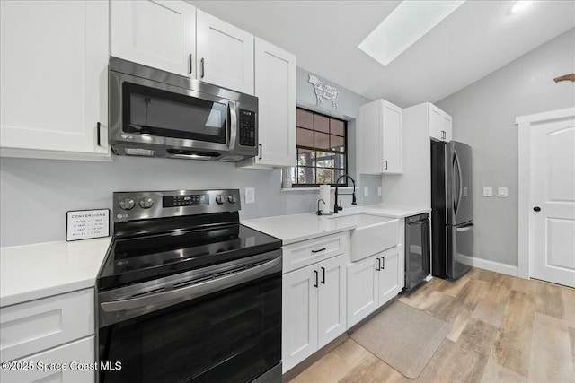 kitchen with sink, appliances with stainless steel finishes, vaulted ceiling with skylight, light hardwood / wood-style floors, and white cabinets