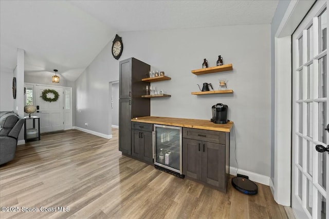 bar with lofted ceiling, dark brown cabinetry, butcher block countertops, light wood-type flooring, and beverage cooler