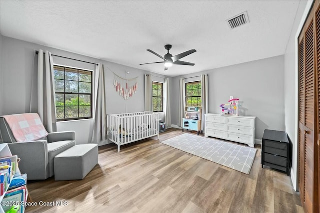 bedroom featuring a nursery area, ceiling fan, a closet, and a textured ceiling