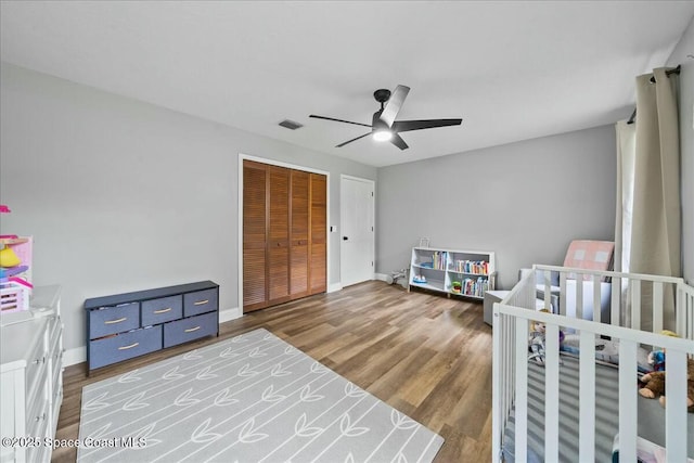 bedroom featuring a nursery area, hardwood / wood-style floors, ceiling fan, and a closet