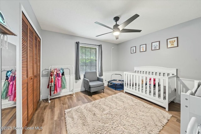 bedroom with a crib, wood-type flooring, ceiling fan, and a closet