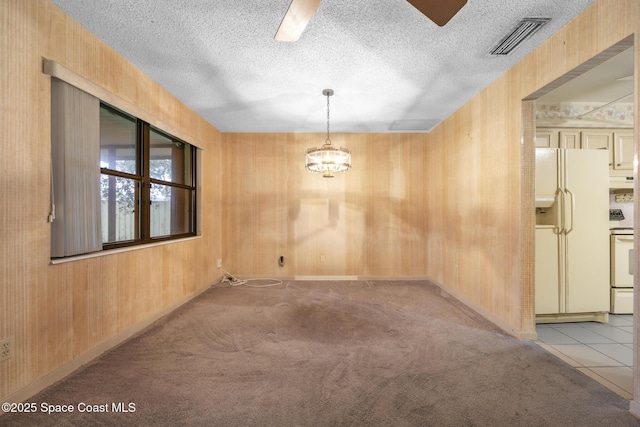 carpeted empty room featuring wooden walls, an inviting chandelier, and a textured ceiling