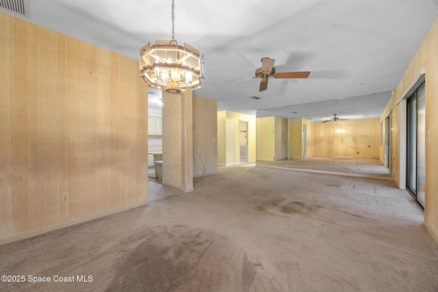 carpeted spare room featuring ceiling fan with notable chandelier and a textured ceiling