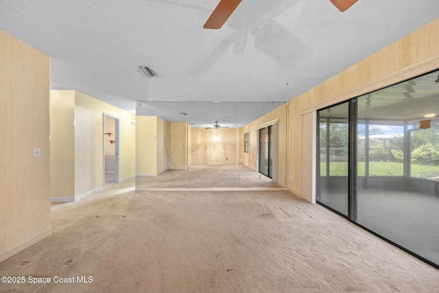 empty room featuring wooden walls, light carpet, a textured ceiling, and ceiling fan