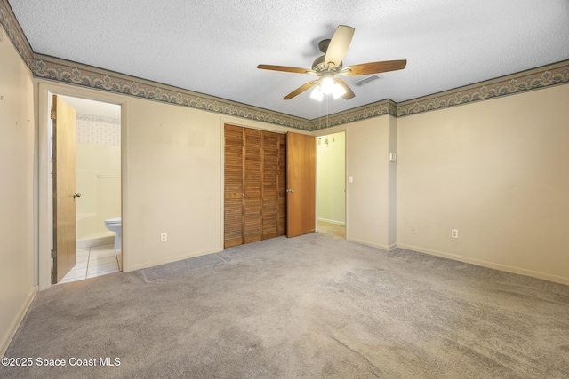 unfurnished bedroom featuring ceiling fan, connected bathroom, a textured ceiling, light colored carpet, and a closet