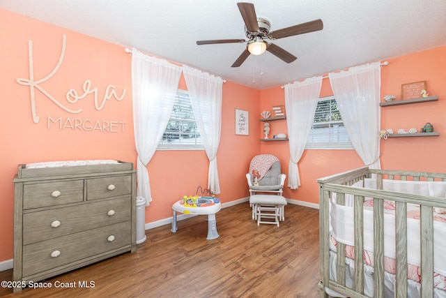 bedroom with a crib, hardwood / wood-style flooring, ceiling fan, and multiple windows