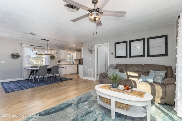 living room with sink, ceiling fan with notable chandelier, a textured ceiling, and light wood-type flooring