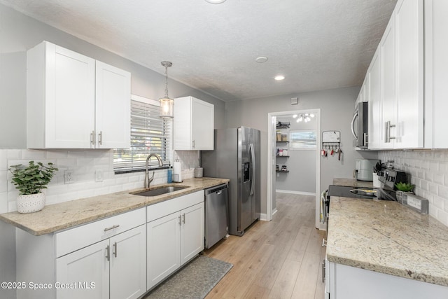 kitchen with appliances with stainless steel finishes, decorative light fixtures, white cabinetry, sink, and light wood-type flooring