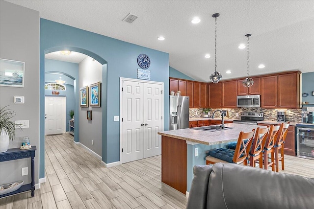 kitchen with lofted ceiling, hanging light fixtures, backsplash, stainless steel appliances, and a center island with sink