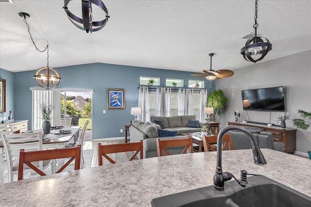 kitchen with sink, vaulted ceiling, hanging light fixtures, a textured ceiling, and ceiling fan with notable chandelier