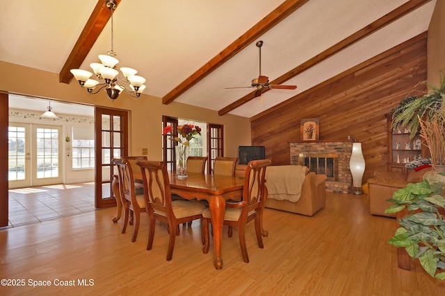 dining space featuring light wood-style flooring, wood walls, french doors, a brick fireplace, and beam ceiling