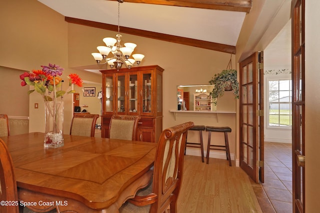 dining space featuring lofted ceiling with beams, light wood-type flooring, baseboards, and an inviting chandelier