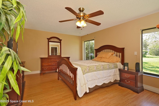 bedroom with ceiling fan, light wood-style flooring, baseboards, and a textured ceiling