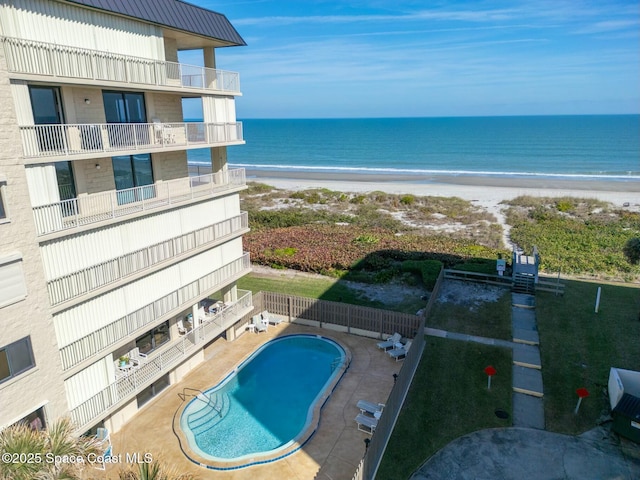 view of swimming pool featuring a water view, a beach view, and a patio area