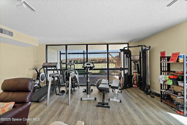 workout area featuring hardwood / wood-style flooring, a wall of windows, and a textured ceiling