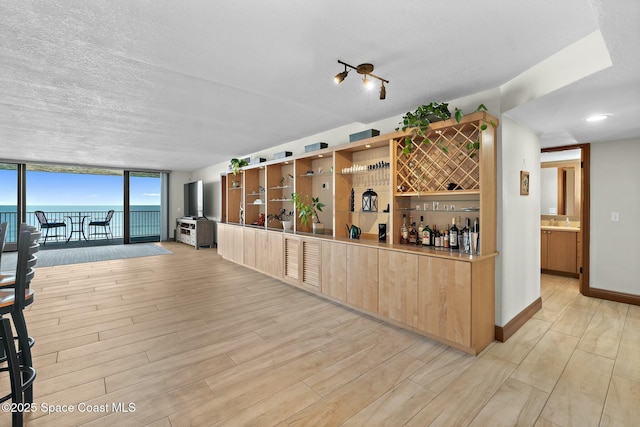 bar featuring light wood-type flooring, a wall of windows, a water view, light brown cabinets, and a textured ceiling