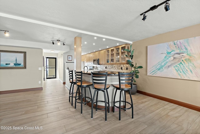 kitchen featuring decorative backsplash, a breakfast bar, a textured ceiling, and light brown cabinets