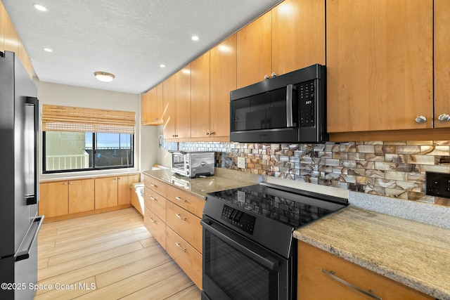 kitchen featuring tasteful backsplash, light wood-type flooring, stainless steel refrigerator, range with electric stovetop, and light stone countertops