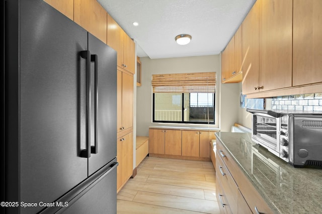 kitchen with fridge, dark stone counters, and tasteful backsplash