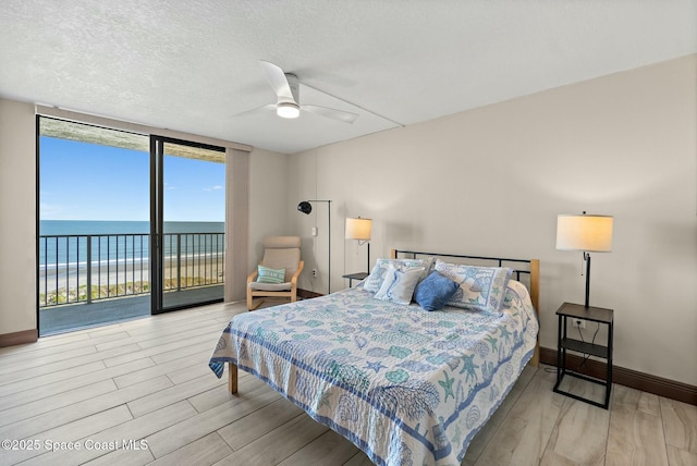 bedroom featuring a water view, floor to ceiling windows, light hardwood / wood-style flooring, and access to outside