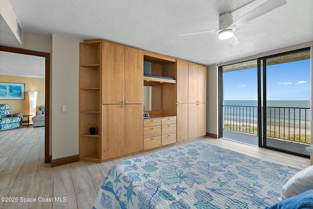 bedroom with a water view, light hardwood / wood-style flooring, a textured ceiling, expansive windows, and access to exterior