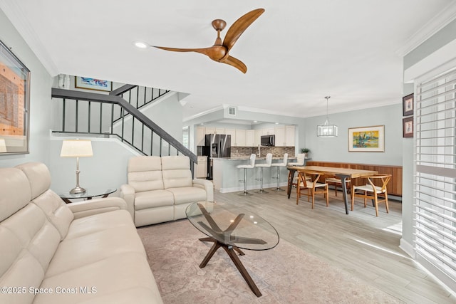 living room with ornamental molding, ceiling fan with notable chandelier, and light hardwood / wood-style flooring