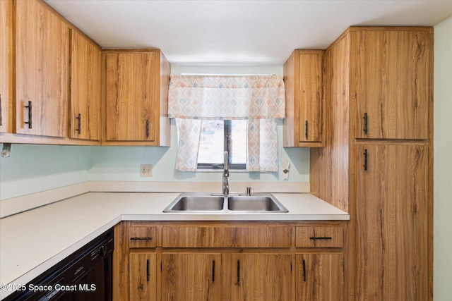 kitchen featuring brown cabinets, light countertops, black dishwasher, and a sink