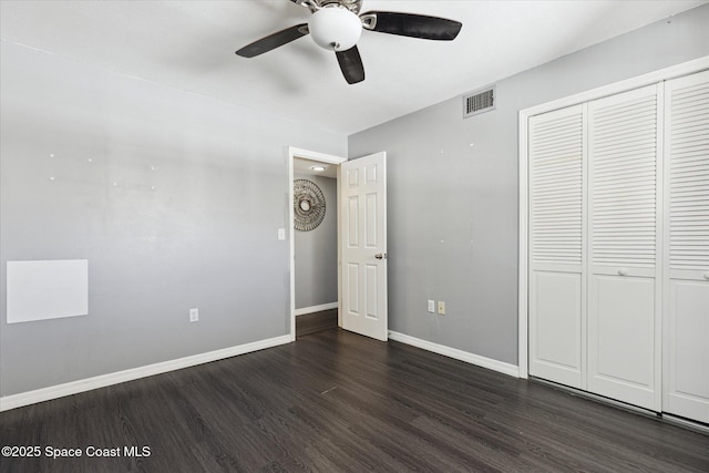 unfurnished bedroom featuring dark wood-style floors, visible vents, baseboards, ceiling fan, and a closet