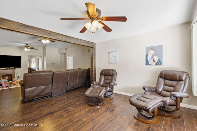 living area with a warm lit fireplace, baseboards, and dark wood-style flooring