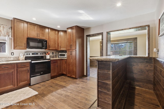 kitchen with a peninsula, stainless steel electric range oven, black microwave, and brown cabinetry