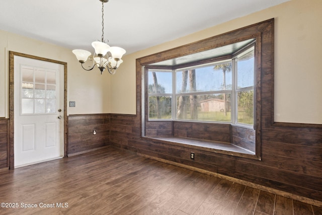 unfurnished dining area with a chandelier, dark wood-style flooring, wainscoting, and wooden walls