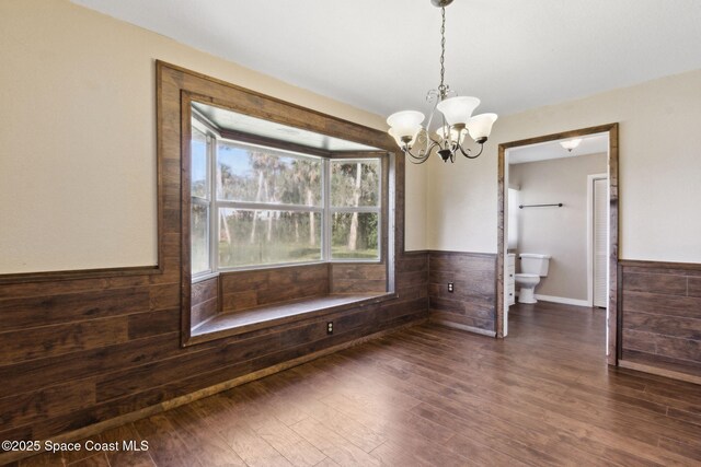 unfurnished dining area with wooden walls, dark wood-type flooring, wainscoting, and an inviting chandelier