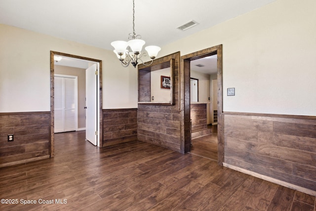 unfurnished dining area featuring a wainscoted wall, dark wood-style floors, visible vents, and a chandelier