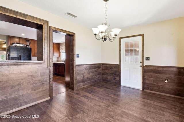 unfurnished dining area with a notable chandelier, visible vents, dark wood-type flooring, wainscoting, and a sink