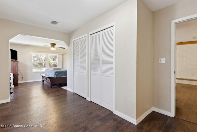 hall featuring dark wood-type flooring, visible vents, and baseboards