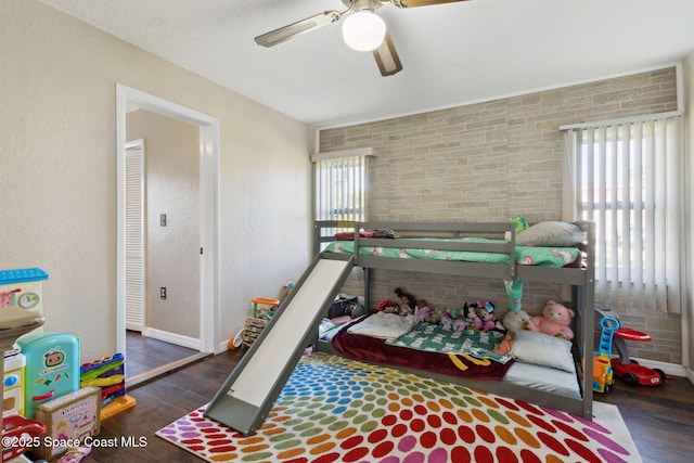 bedroom featuring dark wood-style floors, a textured wall, and a ceiling fan