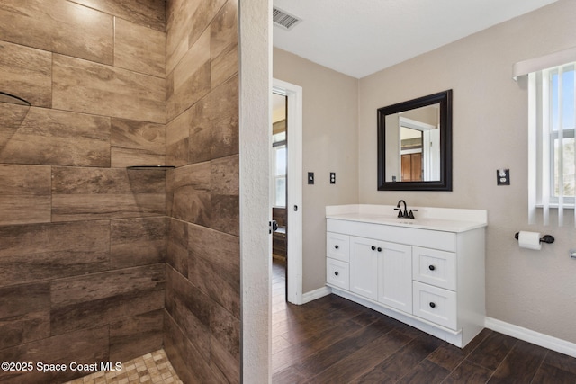 bathroom featuring baseboards, tiled shower, wood finished floors, and vanity