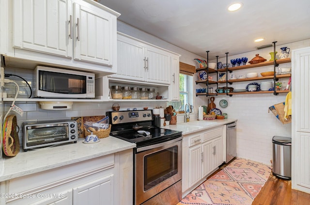 kitchen with sink, stainless steel appliances, light stone counters, white cabinets, and light wood-type flooring