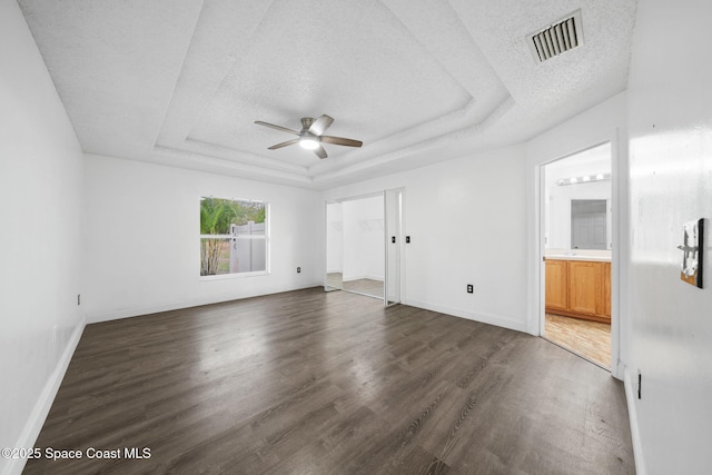 unfurnished room with ceiling fan, a tray ceiling, dark wood-type flooring, and a textured ceiling