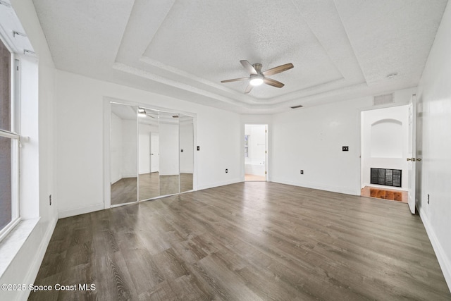 unfurnished living room featuring ceiling fan, hardwood / wood-style floors, a textured ceiling, and a tray ceiling