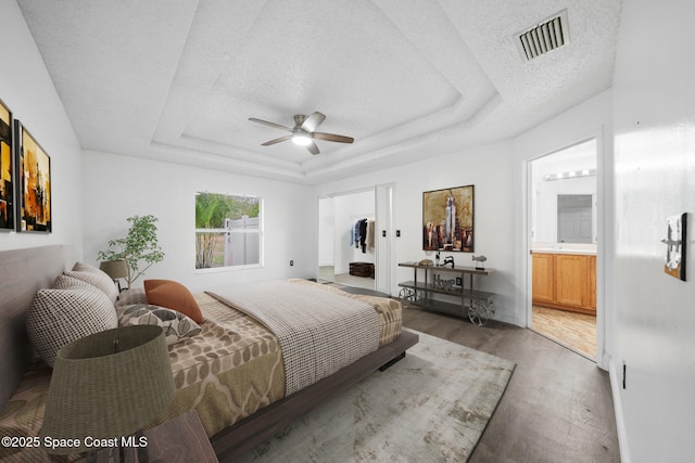 bedroom with ceiling fan, dark wood-type flooring, ensuite bath, and a tray ceiling