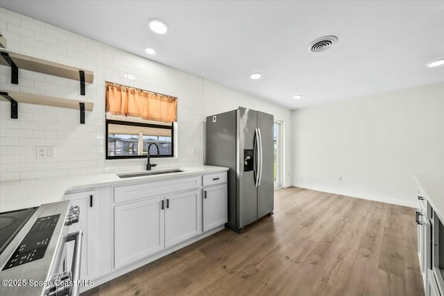 kitchen with sink, white cabinetry, wood-type flooring, stainless steel appliances, and decorative backsplash