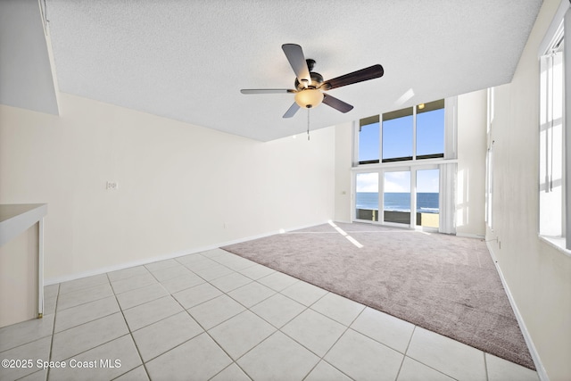 empty room with ceiling fan, a water view, light colored carpet, and a textured ceiling