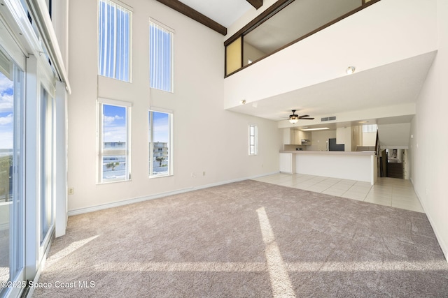 unfurnished living room featuring beamed ceiling, a towering ceiling, light colored carpet, and ceiling fan