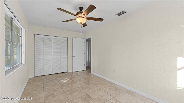 unfurnished bedroom featuring multiple windows, light tile patterned floors, ceiling fan, and a closet