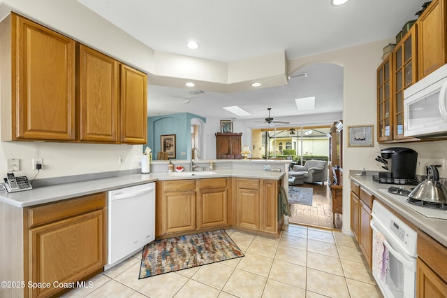 kitchen with sink, white appliances, light tile patterned floors, a skylight, and kitchen peninsula