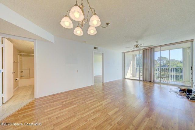 unfurnished room with ceiling fan with notable chandelier, light hardwood / wood-style flooring, expansive windows, and a textured ceiling