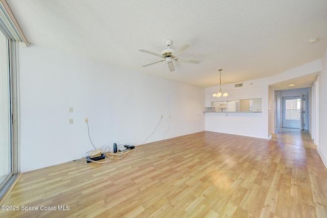 unfurnished living room featuring ceiling fan with notable chandelier and light hardwood / wood-style floors